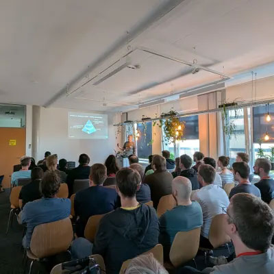 Teilnehmende des CNCF-Meetups bei INFORM in Aachen verfolgen einen Vortrag, auf der Leinwand ist eine Präsentation zu sehen.