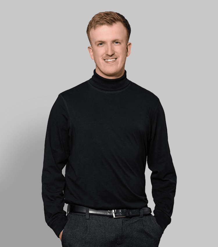 Business woman in a stylish black outfit holding a coffee mug and laptop against a gray background.