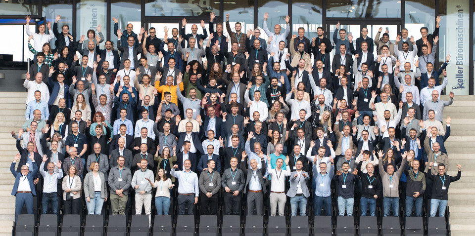 Gruppenfoto mit begeisterten Menschen, die ihre Hände heben, bei einer Veranstaltung im Freien.