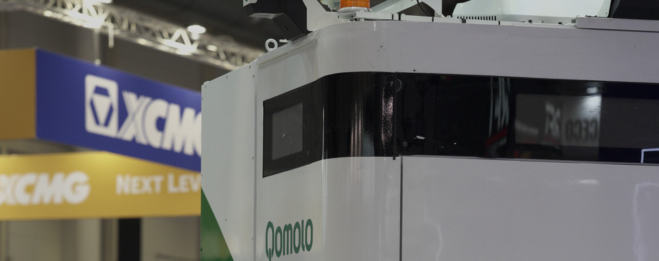 Qomolo electric vehicle display at industry expo, showcasing modern design and innovation in transportation.