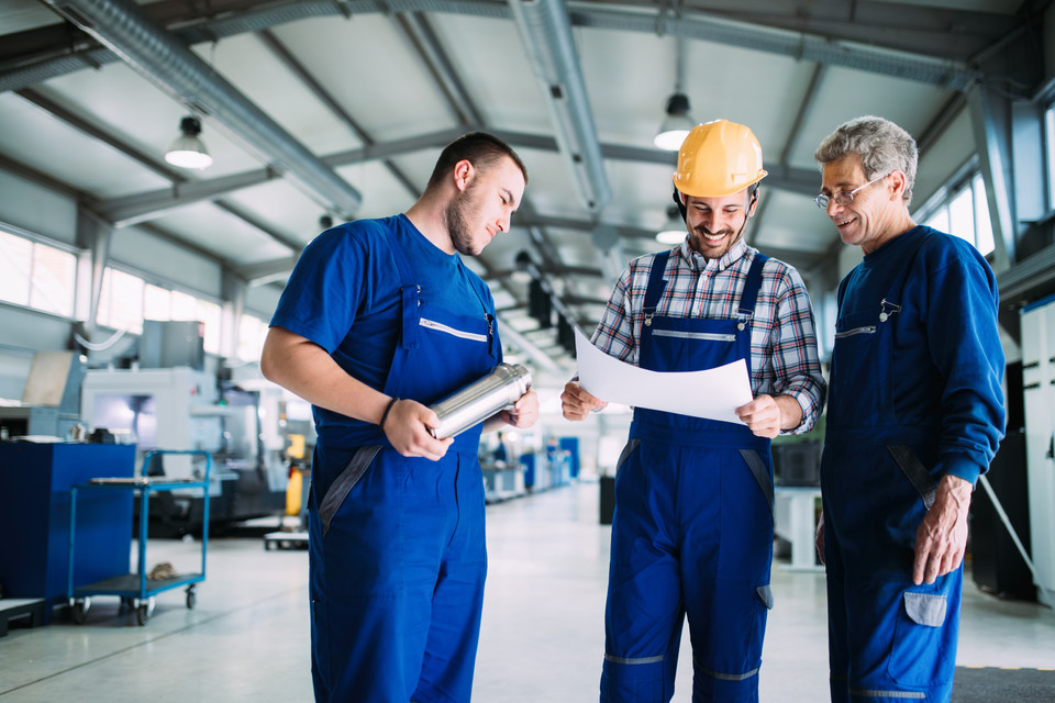 Handwerker in blauer Arbeitskleidung besprechen technische Pläne in einer modernen Werkstatt.