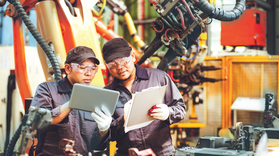 Two workers in front of robot match data on tablet and paper list