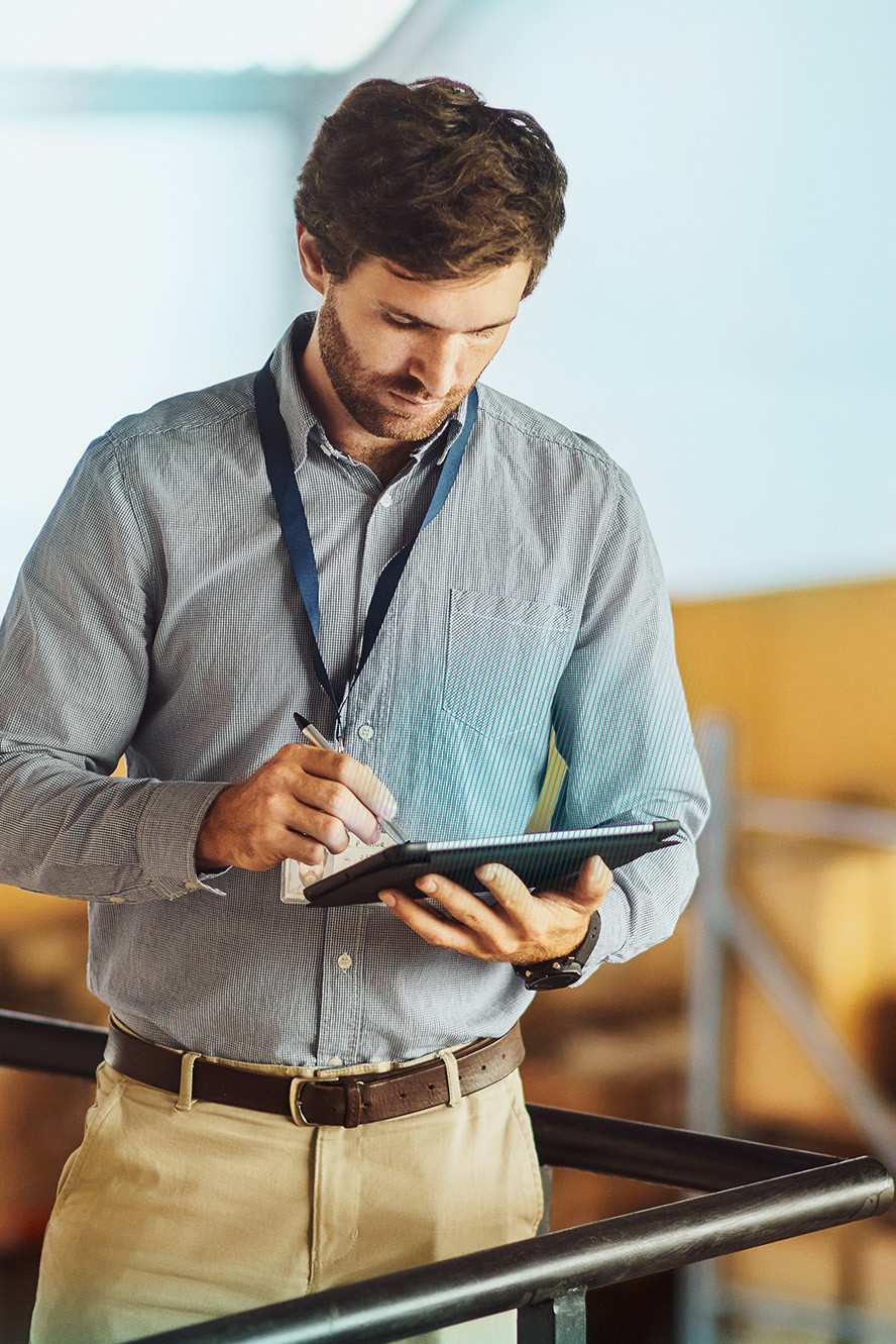 Warehouse manager using a tablet for inventory management among stacked cardboard boxes.