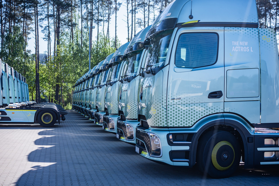 Alt-Tag: "Reihe neuer Mercedes Actros L Lkw in einer sonnigen Umgebung zwischen Bäumen geparkt".