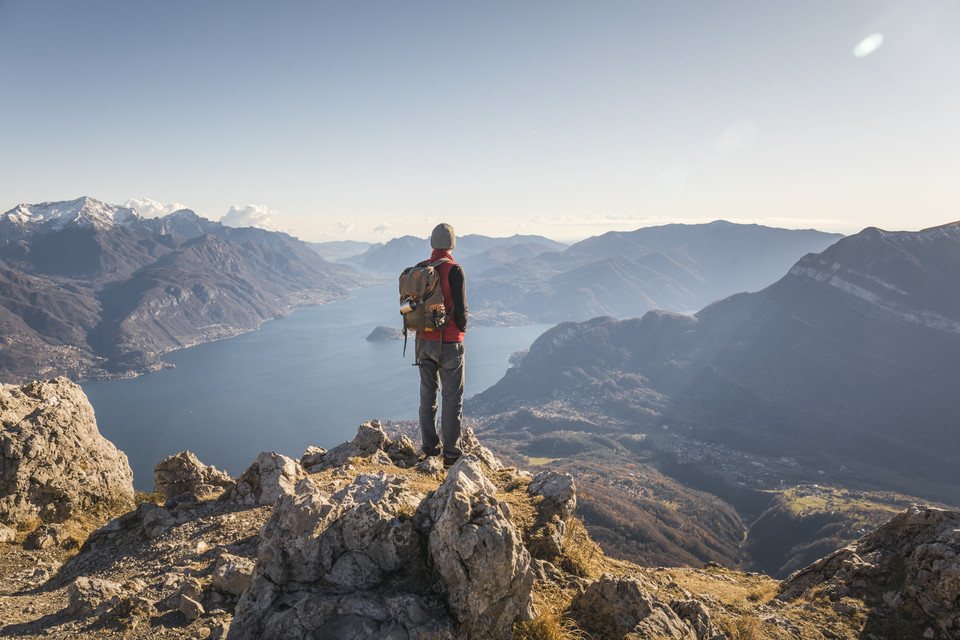 Wanderer mit Rucksack genießt die Aussicht auf den malerischen Lago di Lecco und die umliegenden Berge.