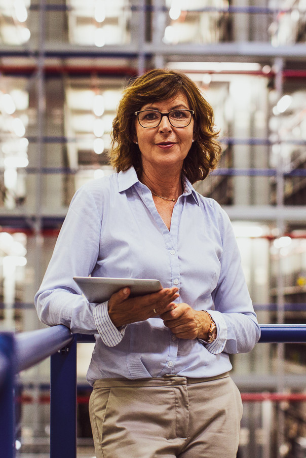 A dispatcher stands in a warehouse holding a tablet with inventory optimization software.
