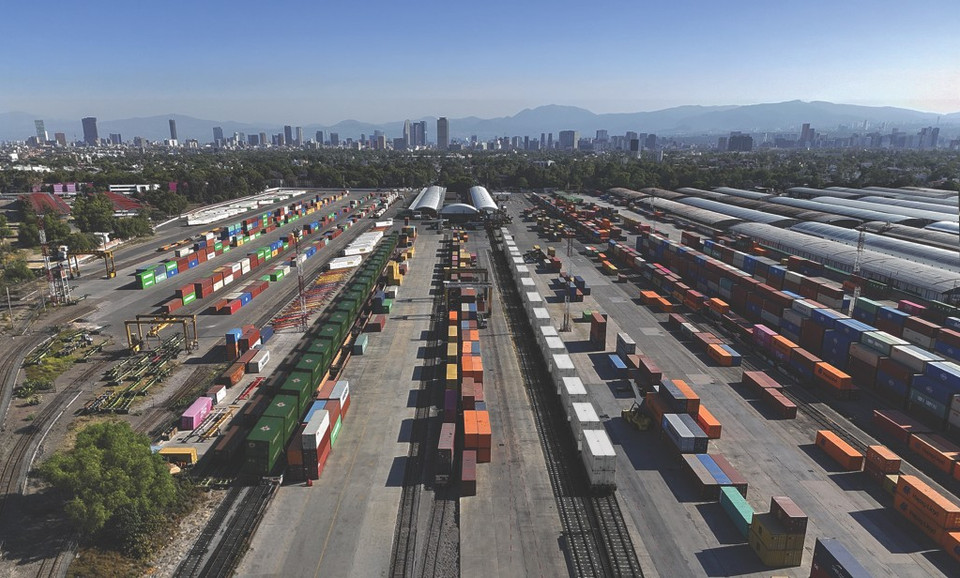 Aerial view of a busy freight yard with colorful shipping containers and a city skyline in the background.
