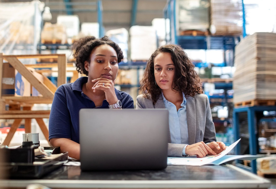 Zwei Frauen analysieren Daten mit Laptop und Dokumenten für den perfekten Schichtplan.