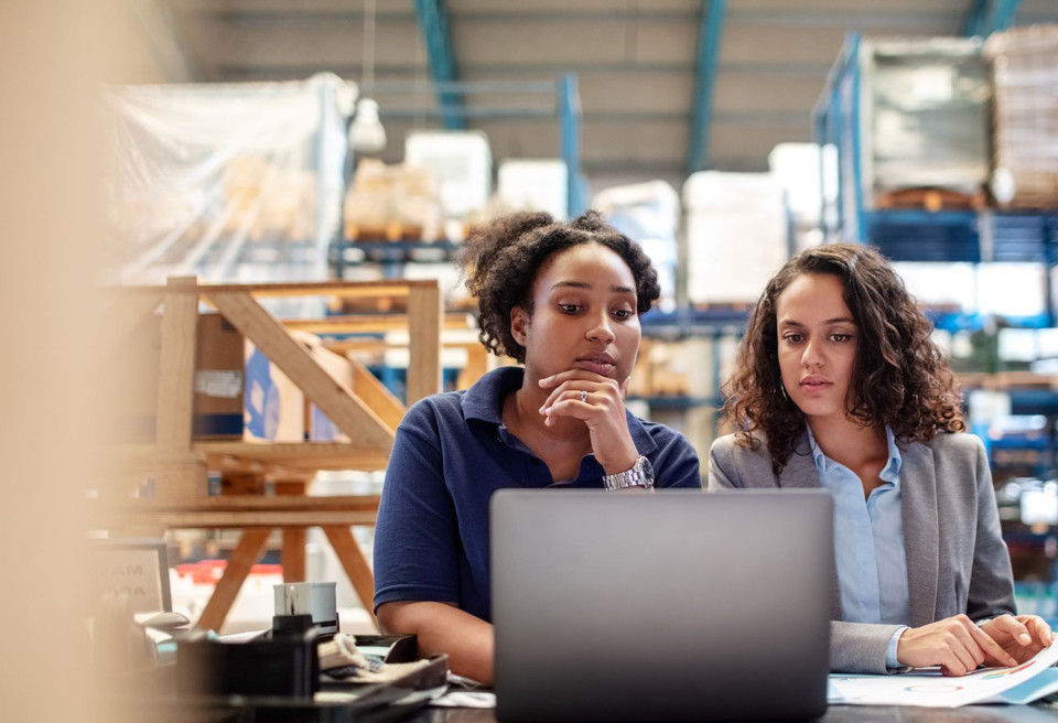 Zwei Frauen analysieren Daten mit Laptop und Dokumenten für den perfekten Schichtplan.