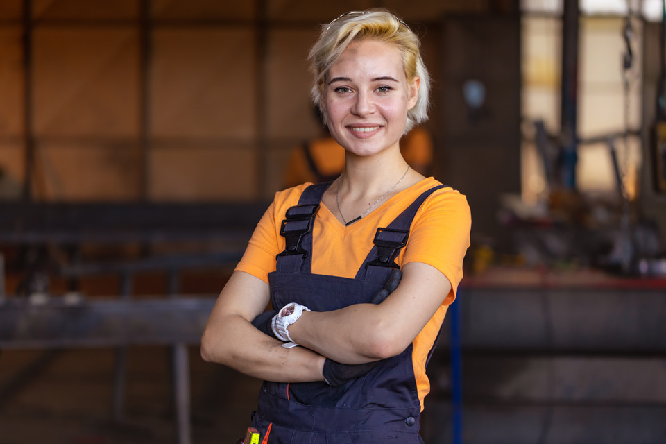 Facharbeiter in Arbeitskleidung mit verschränkten Armen, bereit für die Herausforderungen in der Werkstatt.