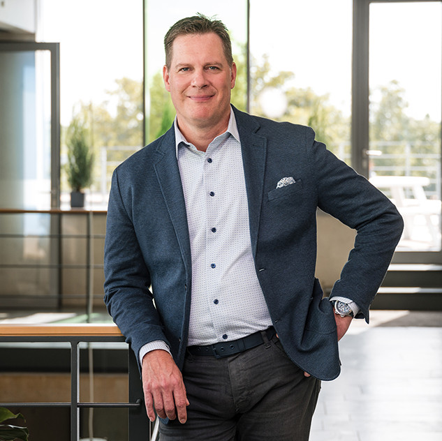 Professional man in a blazer poses confidently in a modern office environment with natural light.