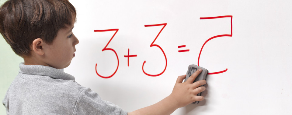 Ein Kind wischt mit einem Schwamm an einer Tafel, auf der 3 + 3 = 7 geschrieben steht.