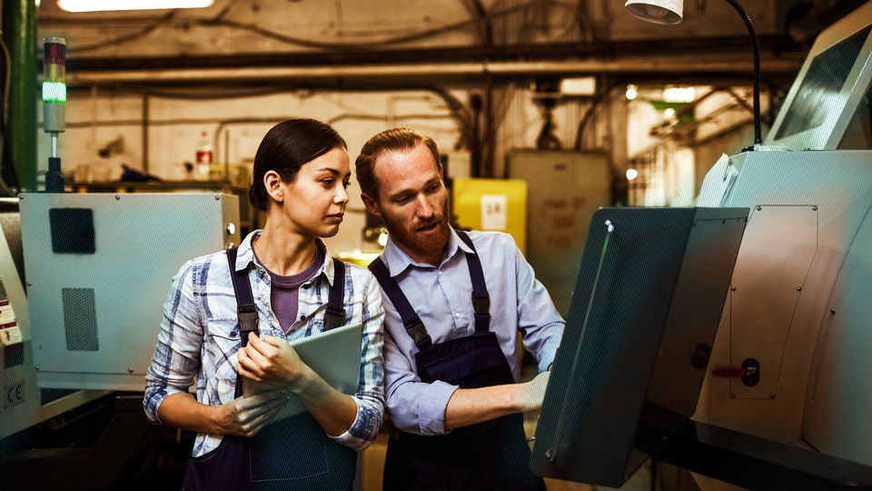 Frau und Mann in der Produktionshalle an einem Bedienpanel