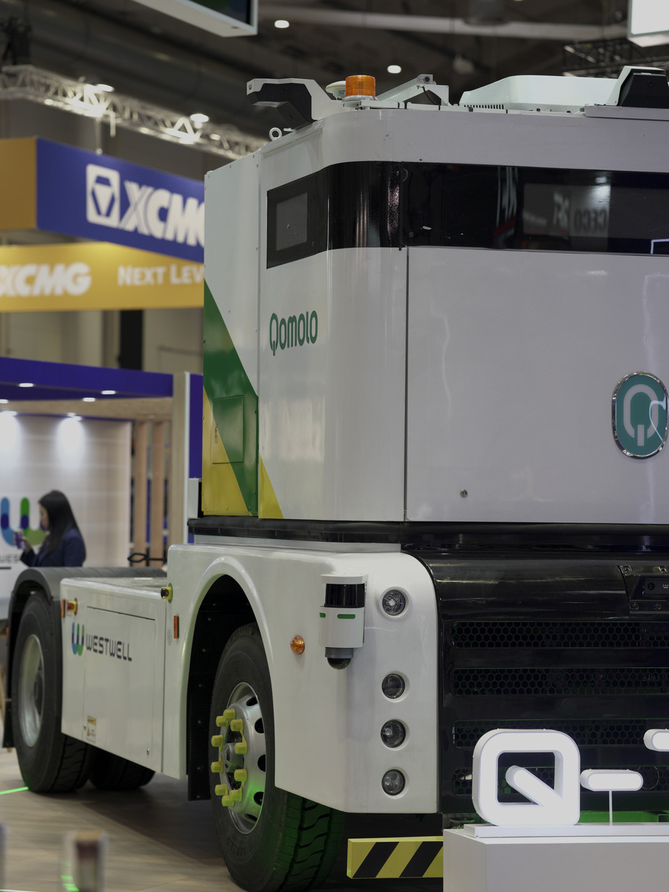 Qomolo electric vehicle display at industry expo, showcasing modern design and innovation in transportation.