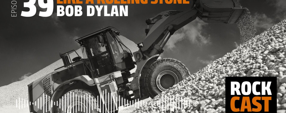 An Excavator driving on a pile of Gravel. Overlay text reads "Episode 39 Like a Rolling Stone Bob Dylan."