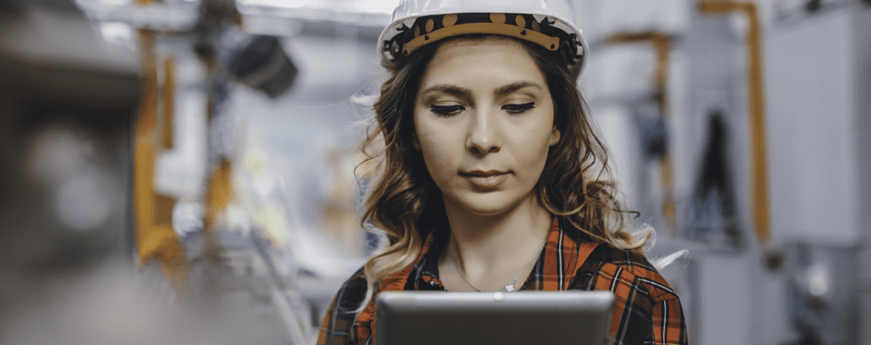 Gen Z Mitarbeiterin in einem Sicherheitshelm, die auf ihrem Tablet ihren Schichtplan aufruft.