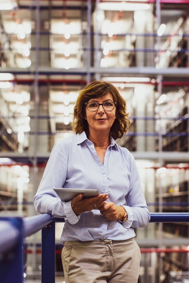 Eine Disponentin steht in einem Lager und hält ein Tablet mit Software zur Bestandsoptimierung.