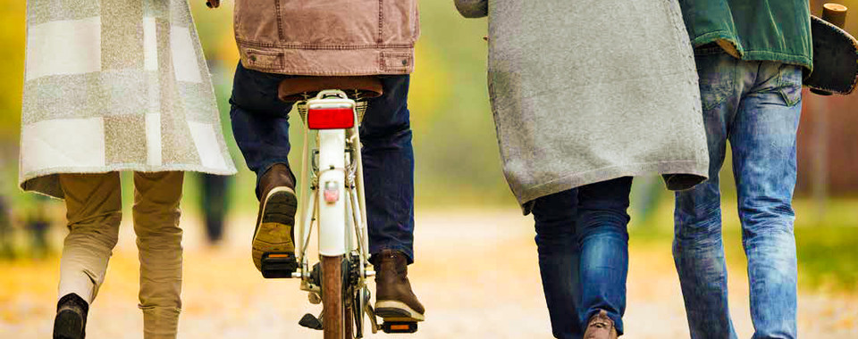 Friends walking together on a path, with one riding a bike, enjoying a vibrant autumn day outdoors.