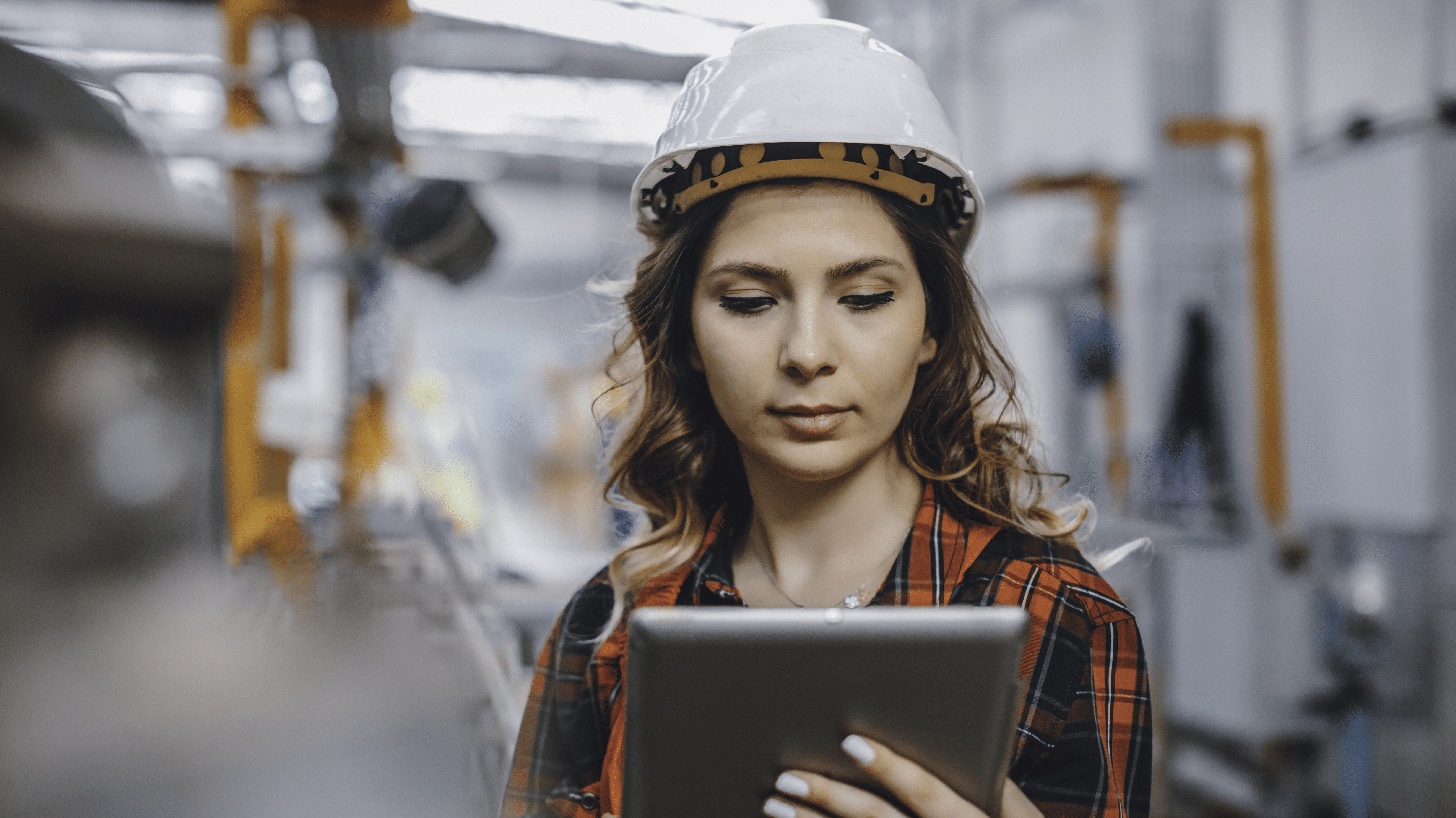 Gen Z Mitarbeiterin in einem Sicherheitshelm, die auf ihrem Tablet ihren Schichtplan aufruft.