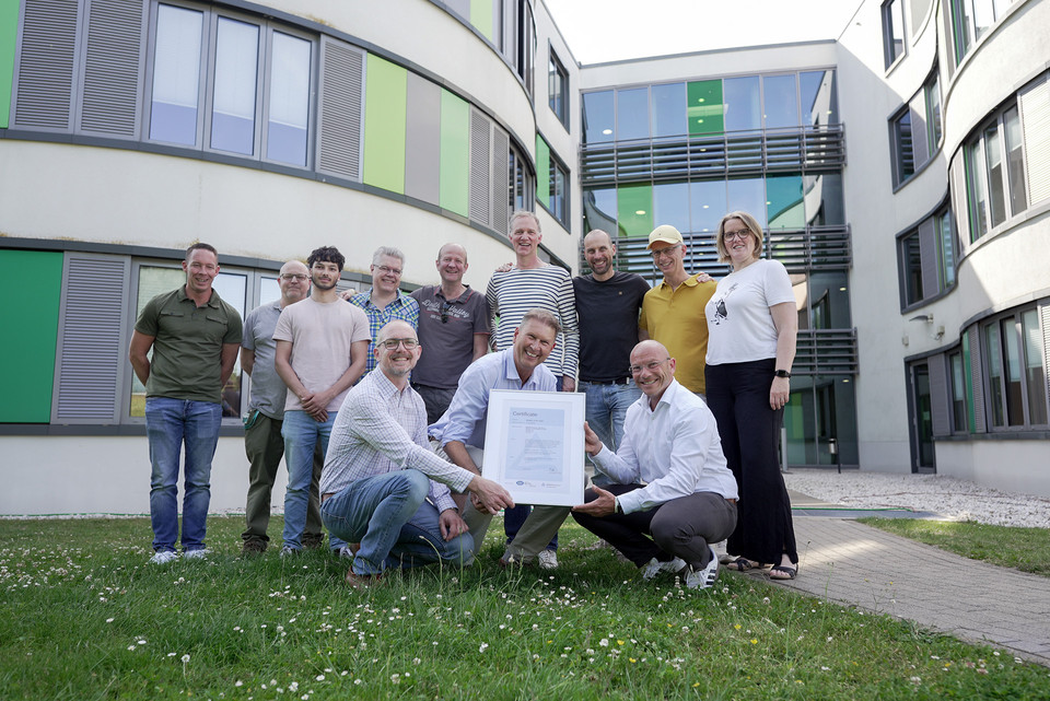 Group celebration outdoors showcasing a certificate in front of a modern building.