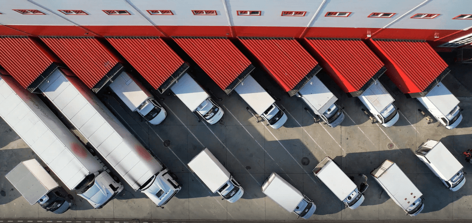 Aerial view of trucks parked at a loading dock with red awnings at a logistics facility. Efficient transport operations.