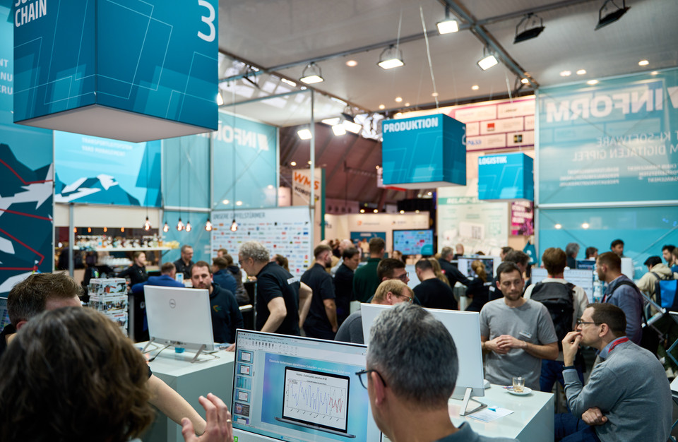 Messestand mit Fachbesuchern, die sich über Produktion und Logistik informieren, bei einer Branchenmesse.
