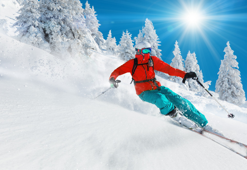 Skifahrer in leuchtender Ausrüstung genießt den frischen Pulverschnee unter sonnigem Himmel.