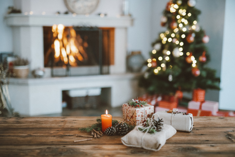 Gemütliche Weihnachtsstimmung mit Geschenken, Kerze und Festtagsdekoration vor dem Kamin und Weihnachtsbaum.