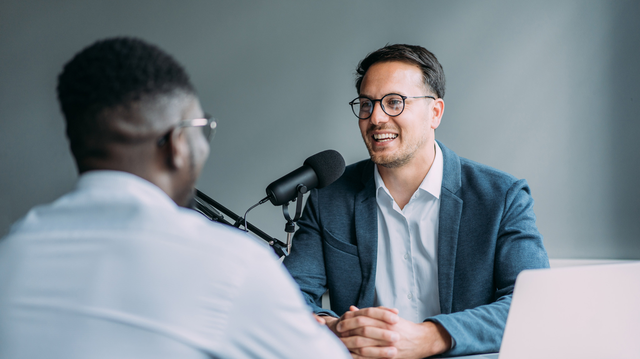 Zwei Männer bei einem Podcast-Interview mit Mikrofon und Laptop in einem modernen Raum.