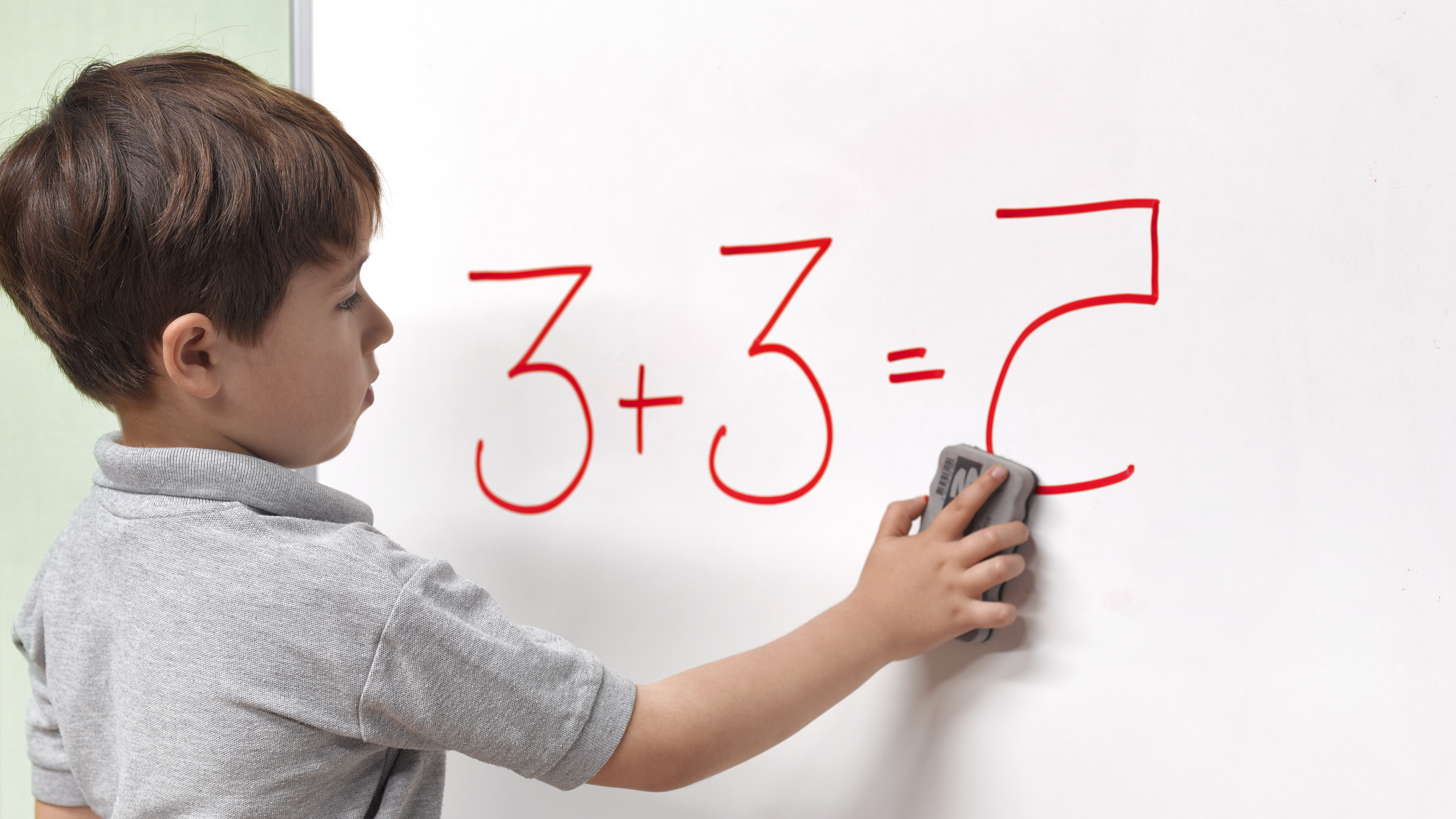A child wipes a sponge on a blackboard on which 3 + 3 = 7 is written.
