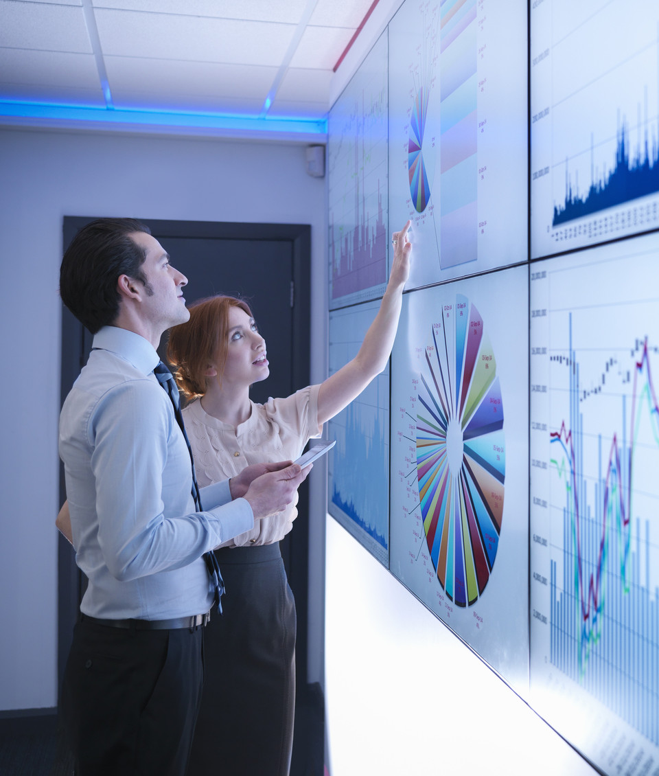 Woman and man stand in front of digital screens that display data