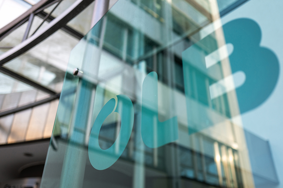 Glasfassade eines modernen Bürogebäudes mit reflektiertem OLB-Logo im Vordergrund