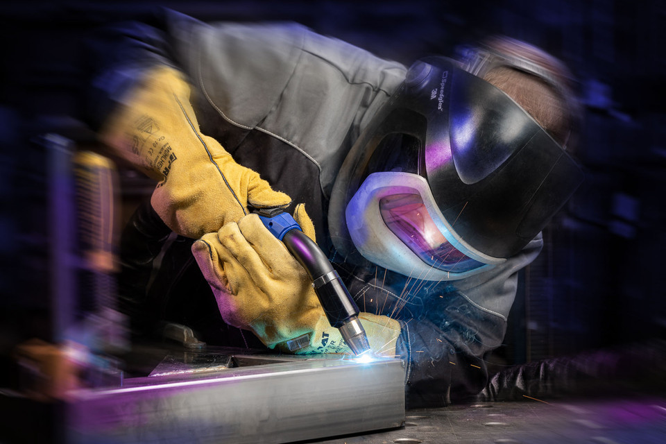 Schweißer mit Schutzausrüstung in Aktion, der Metall mit präziser Technik bearbeitet.