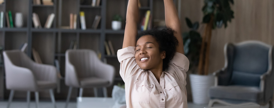Happy woman stretching at her desk in a cozy modern office, promoting wellness and work-life balance.
