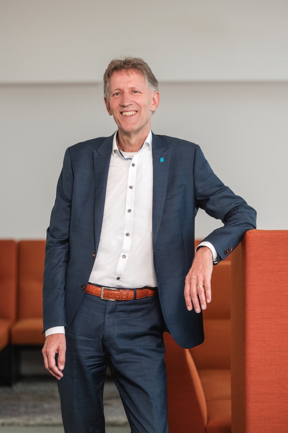 Business professional in a suit leaning on a chair in a modern office setting, embodying confidence and approachability.