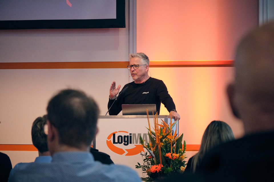 Redner präsentiert auf der LogiMAT 2023, im Hintergrund Publikum und blühende Arrangements.