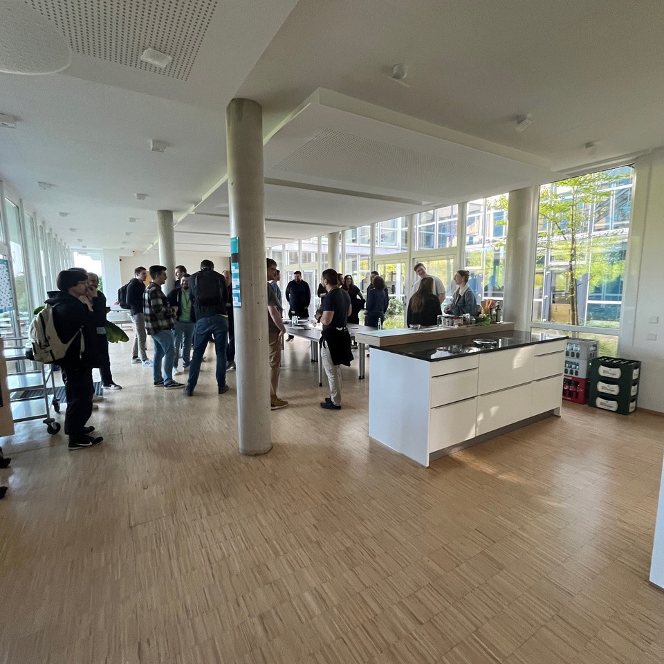 Gäste des CNCF-Meetups bei INFORM stehen in einem lichtdurchfluteten Raum und tauschen sich bei Snacks und Drinks aus.