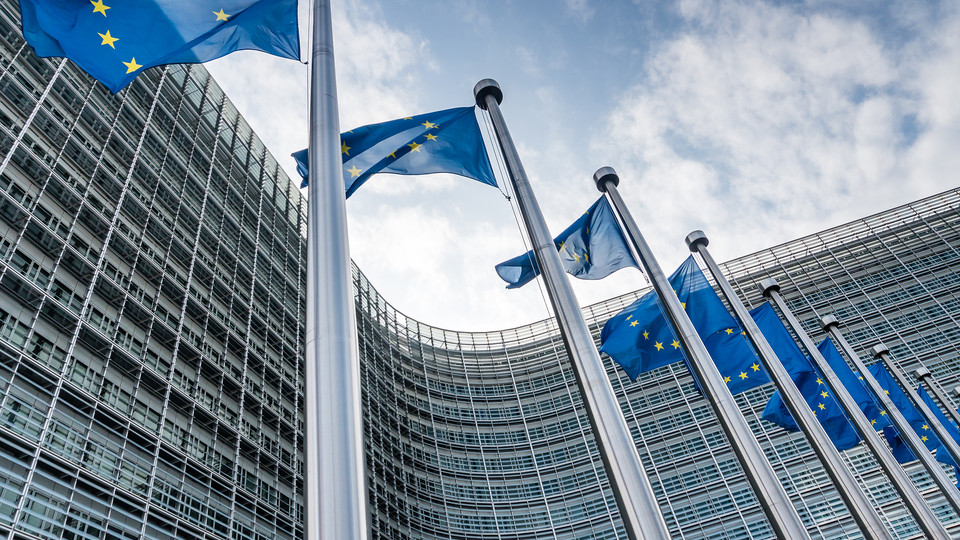 EU-Flaggen vor dem Gebäude der Europäischen Kommission in Brüssel, symbolisieren Einheit und Zusammenarbeit in Europa.
