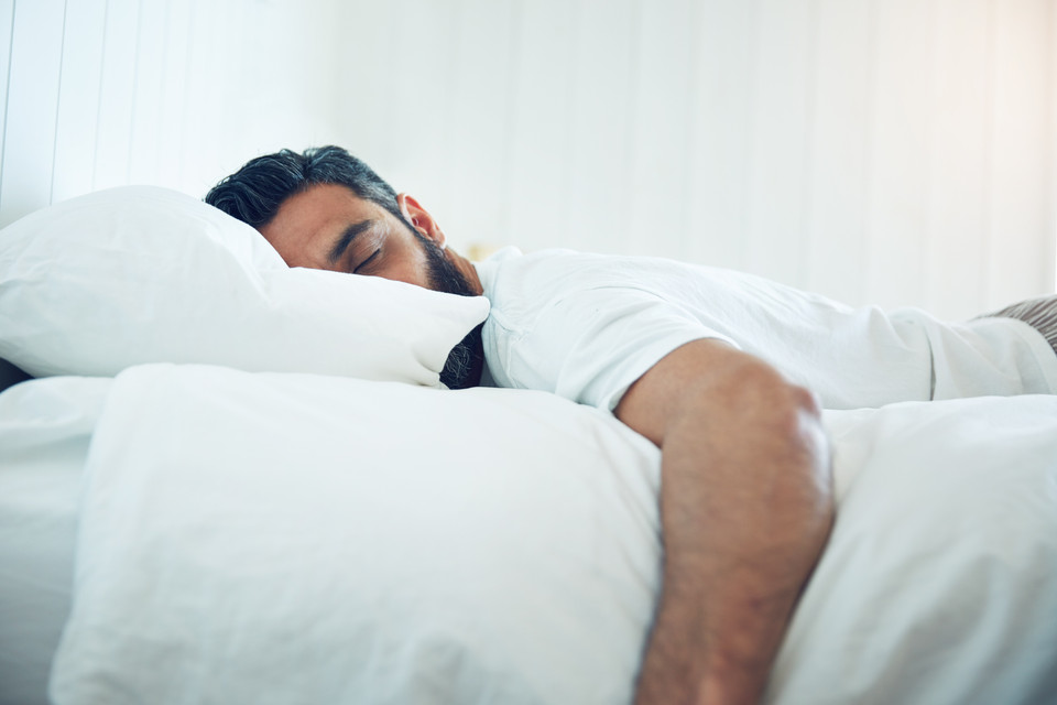 Entspannter Mann, der auf einem Bett mit weißen Kissen liegt, ideal für Artikel über Schlaf und Erholung.