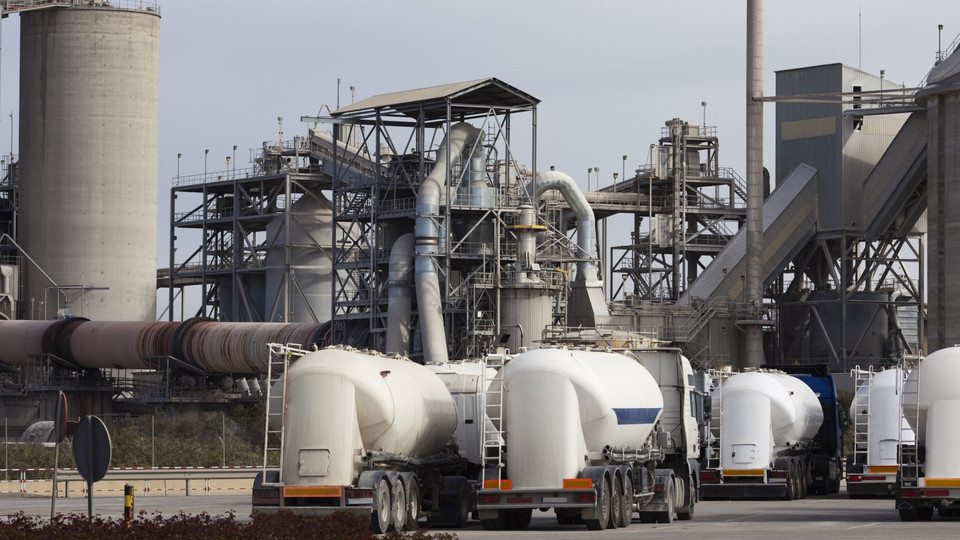 Industrial cement plant with large silos and concrete mixer trucks in the foreground on a cloudy day.
