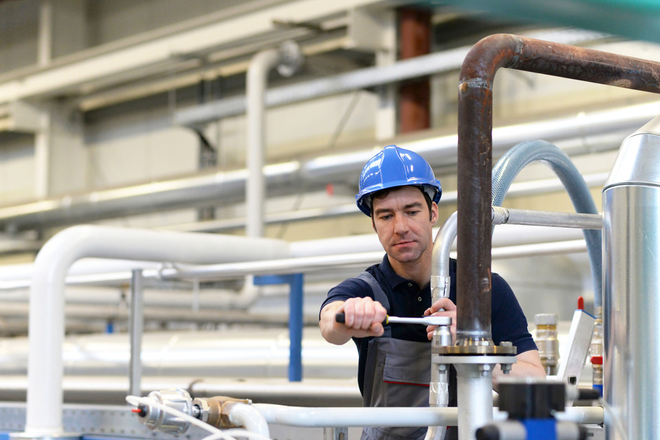 Techniker mit Blauhelm arbeitet an Industrieanlagen in einer modernen Fertigungsumgebung.