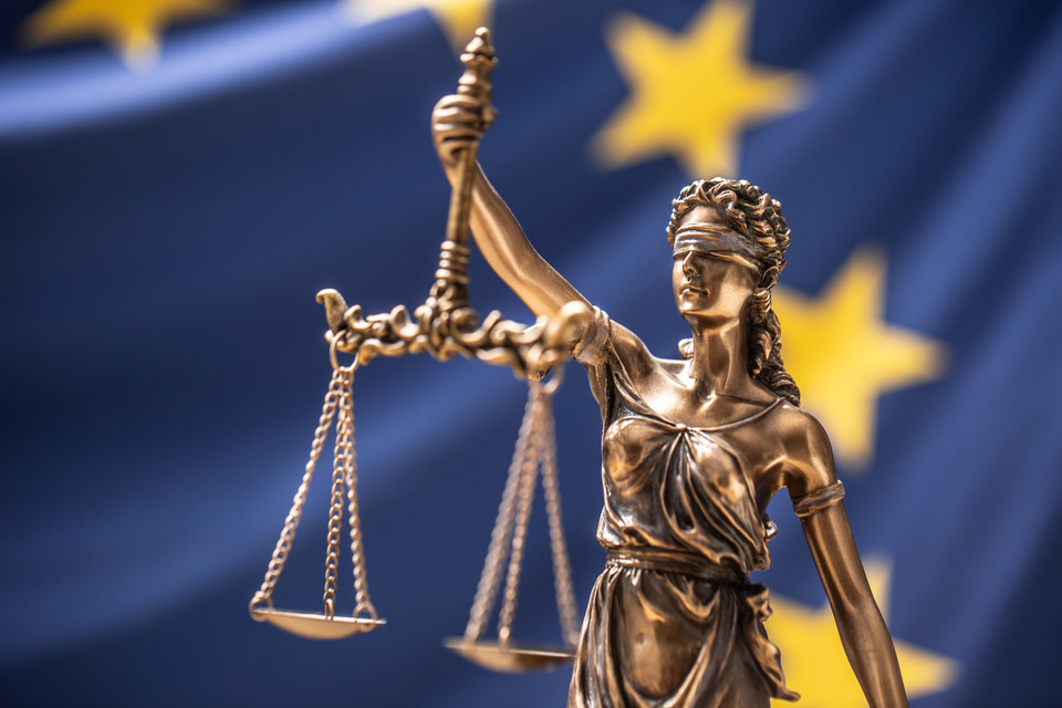 Statue der Justitia mit Waage vor der EU-Flagge, Symbol für Recht und Gerechtigkeit in der Europäischen Union.
