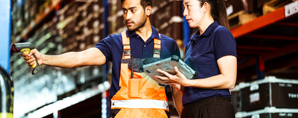 Warehouse workers using a barcode scanner and tablet to manage inventory efficiently in a storage facility.